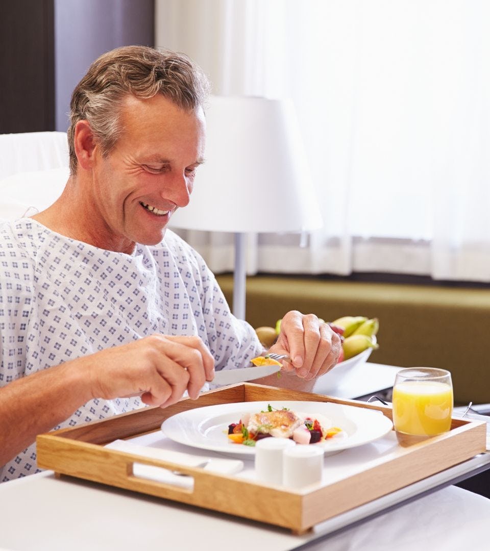 one male lying in hospital bed eating served food