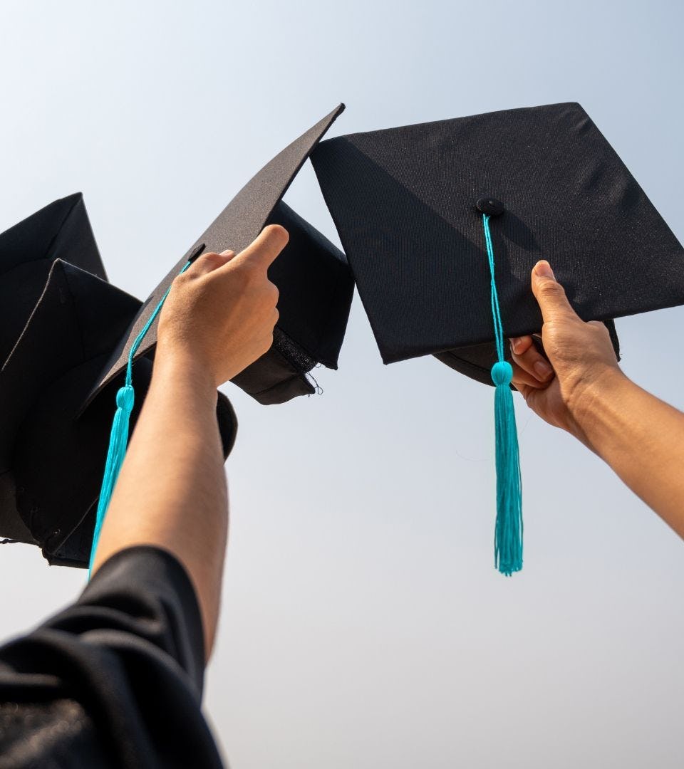 2 hands holding black graduation hats
